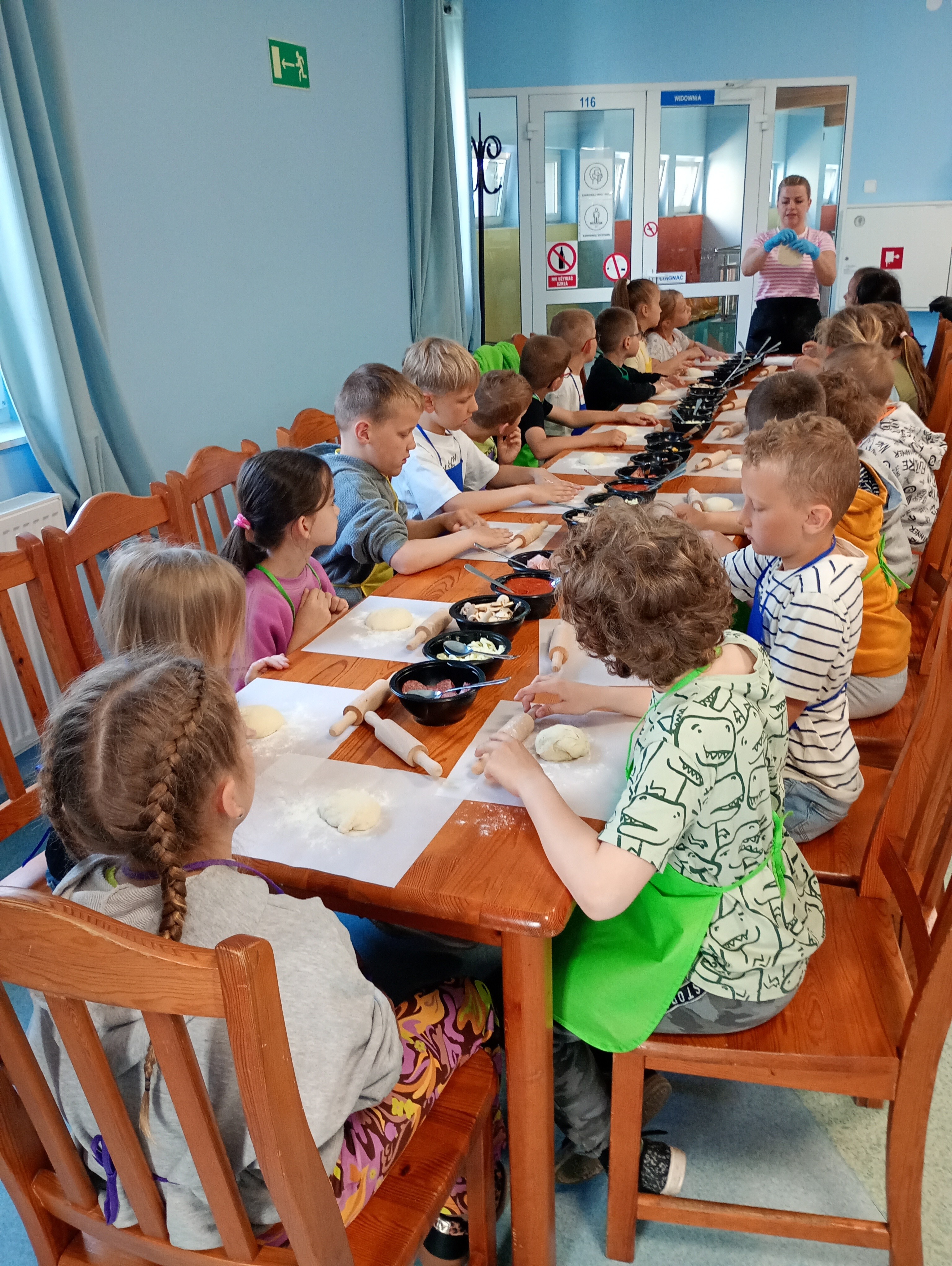 Uczniowie przy stole z produktami niezbędnymi do przygotowania pizzy