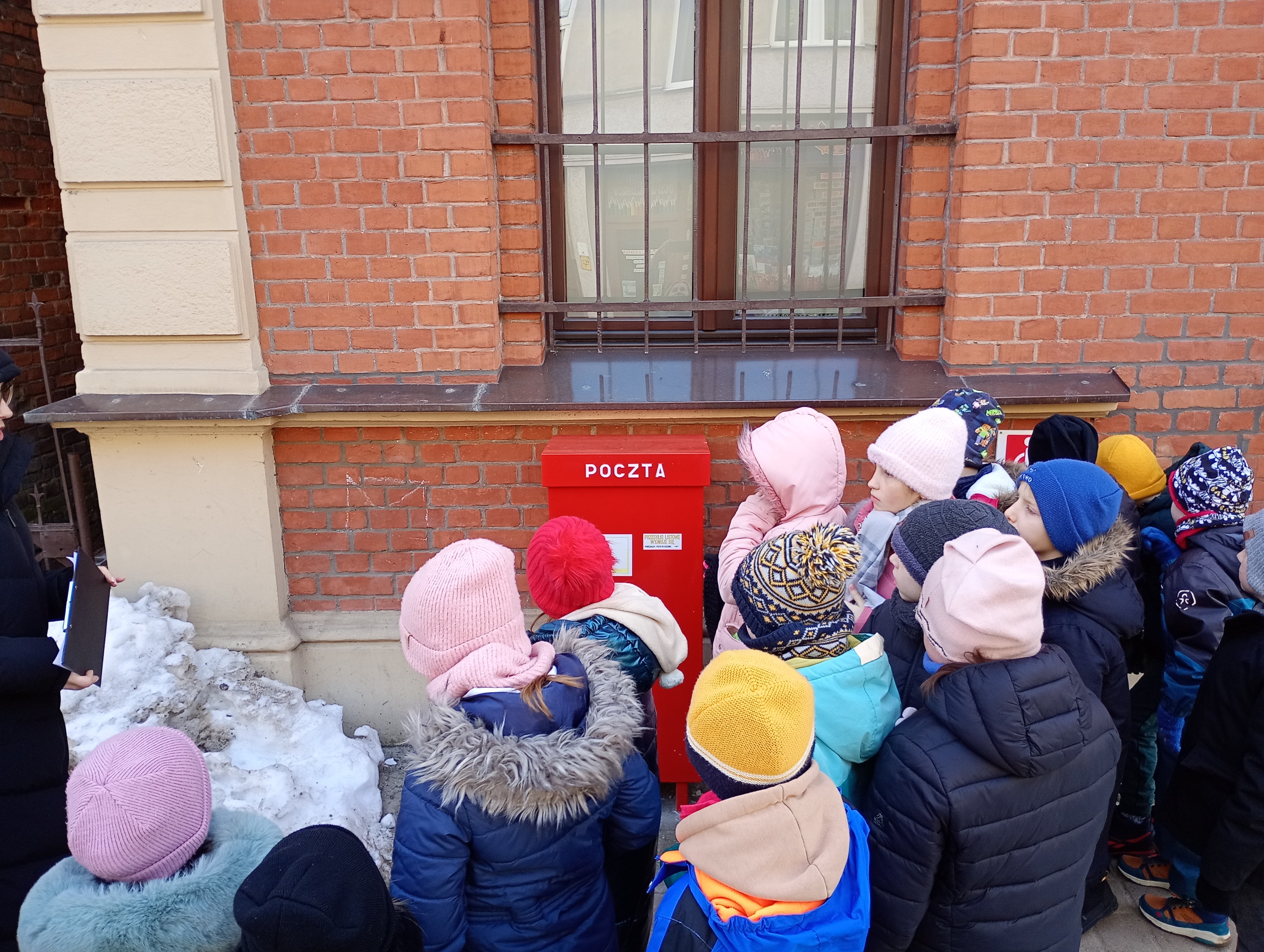 Dzieci stojące obok budynku Poczty Polskiej przy skrzynce pocztowej